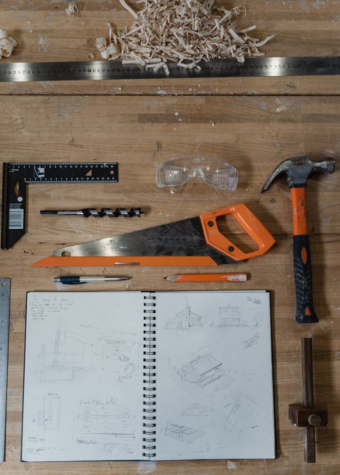client-stories-img Flatlay of carpentry tools and a sketch notebook on a wood workbench.